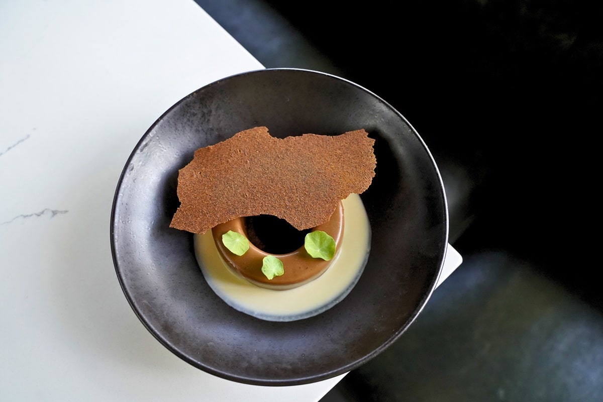 a photo of a piece of tiramisu at Eden in Chicago in a black plate on a white table