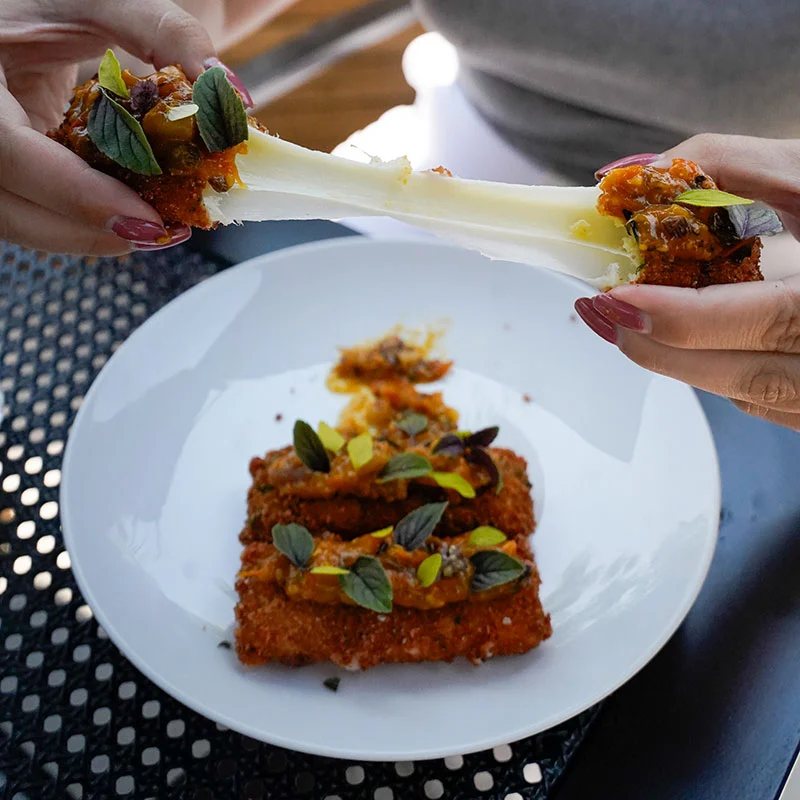 A person pulls apart a piece of the new Mozzarella Sticks on eden's chicago summer 2025 happy hour menu, topped with ramp & sungold tomato salsa, showing a long stretch of melted cheese.